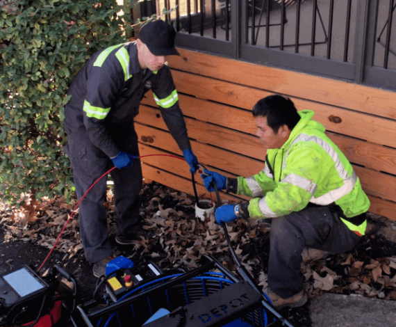 Prodigy Sewer and Drain technicians repair an outdoor sewer line using equipment, carefully completing the job together.